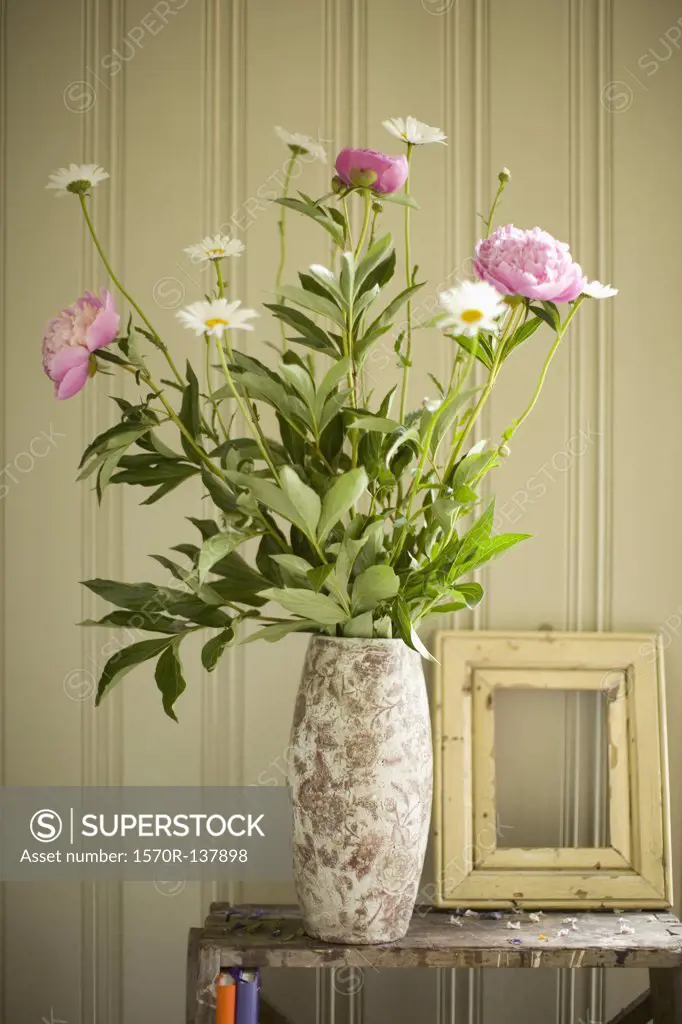 A vase of peonies and daisies and an empty picture frame