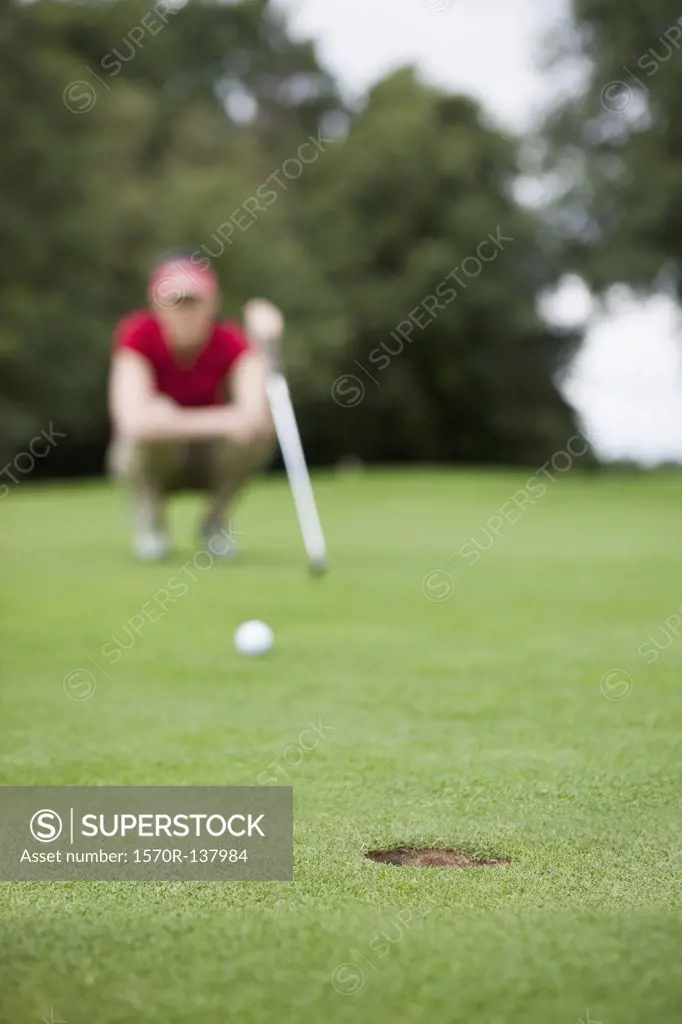 A golfer crouching down studying the distance to the hole, focus on hole