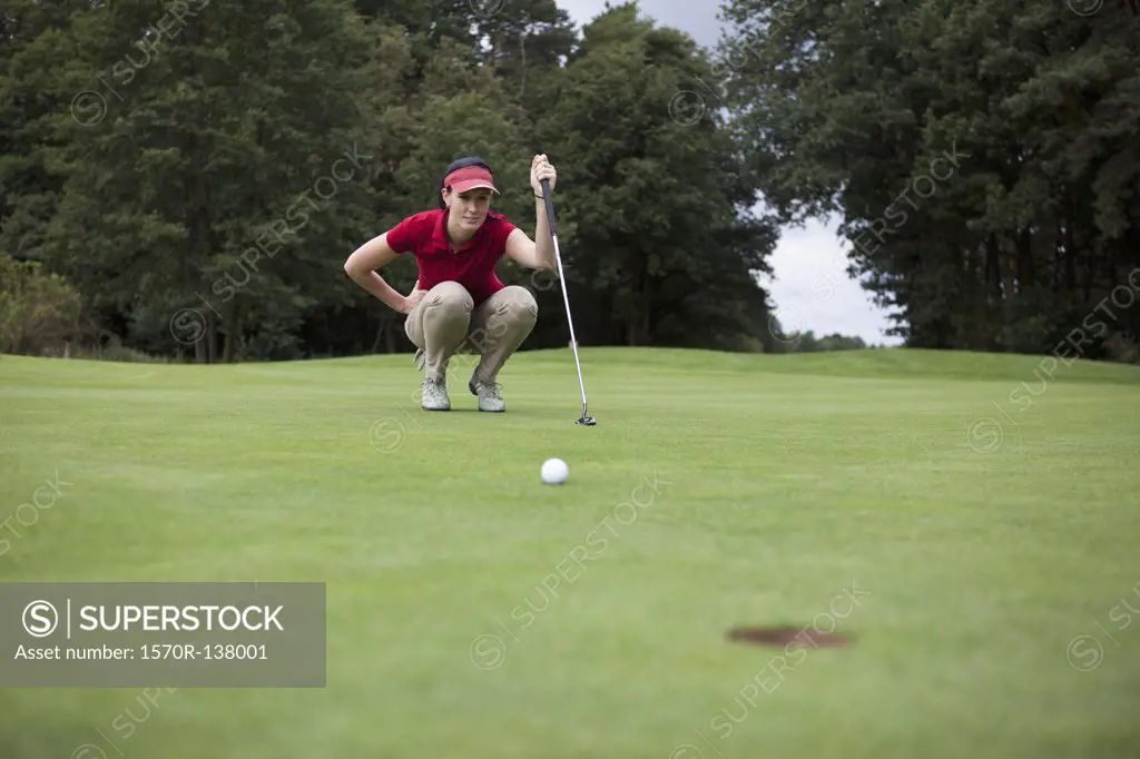 A female golfer crouching down studying the distance to the hole