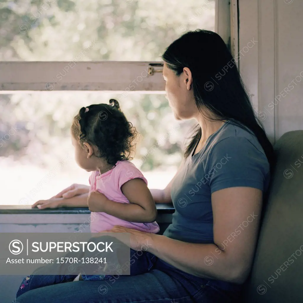 A mother and daughter on a train, looking through window