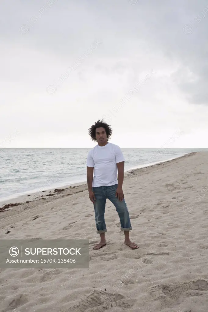 A cool young man standing on a beach, front view