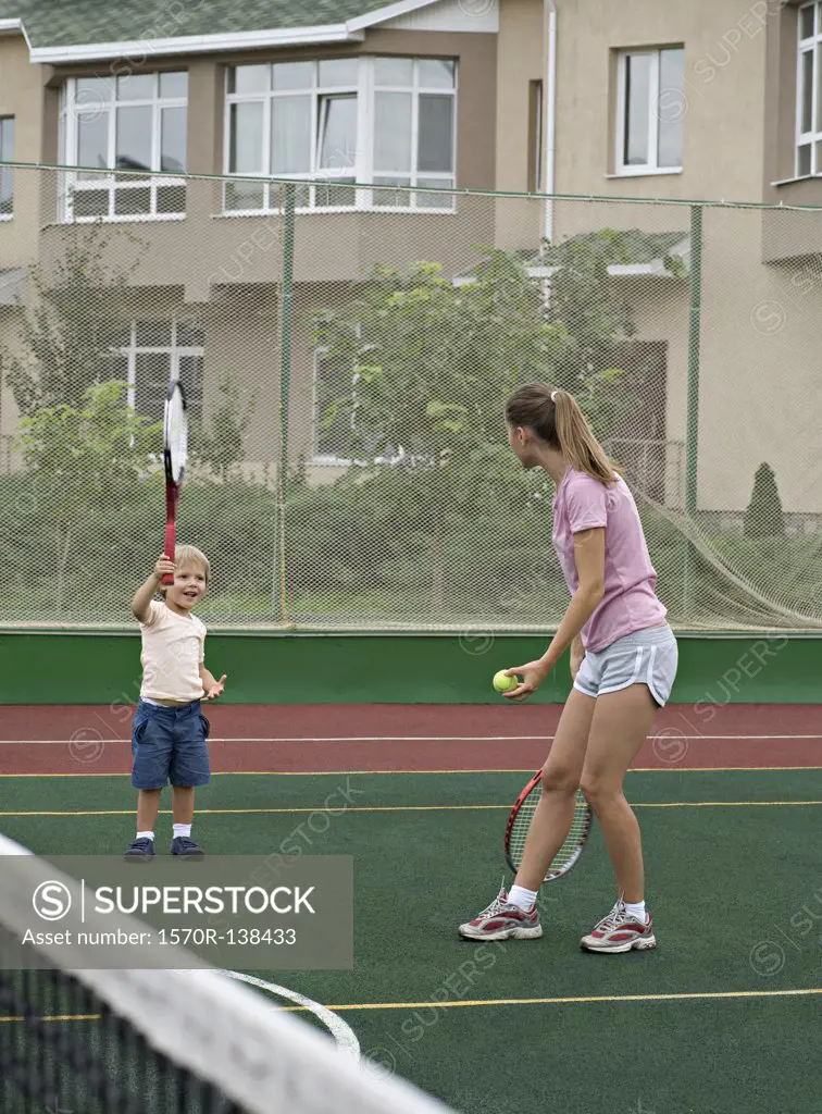 A mother preparing to serve a tennis ball to her young son