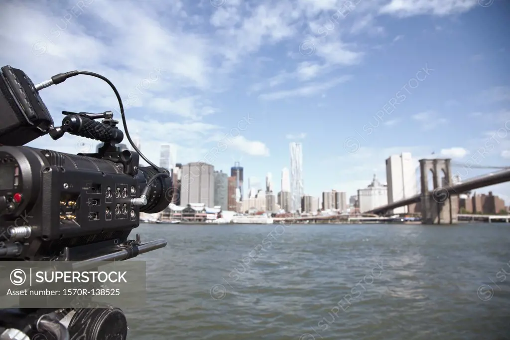 A television camera filming the Brooklyn Bridge and Manhattan skyline