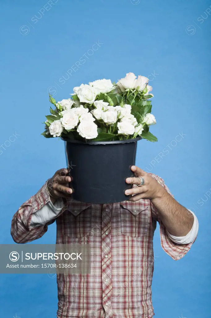 Man holding black bucket of flowers in front of his face