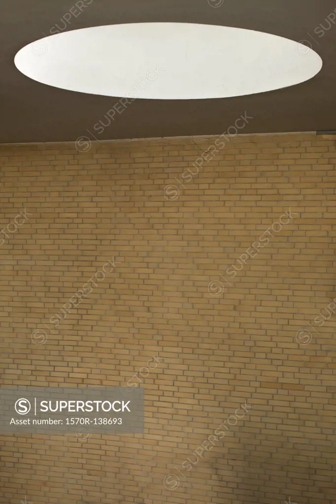 Oval light on ceiling over blank brick wall