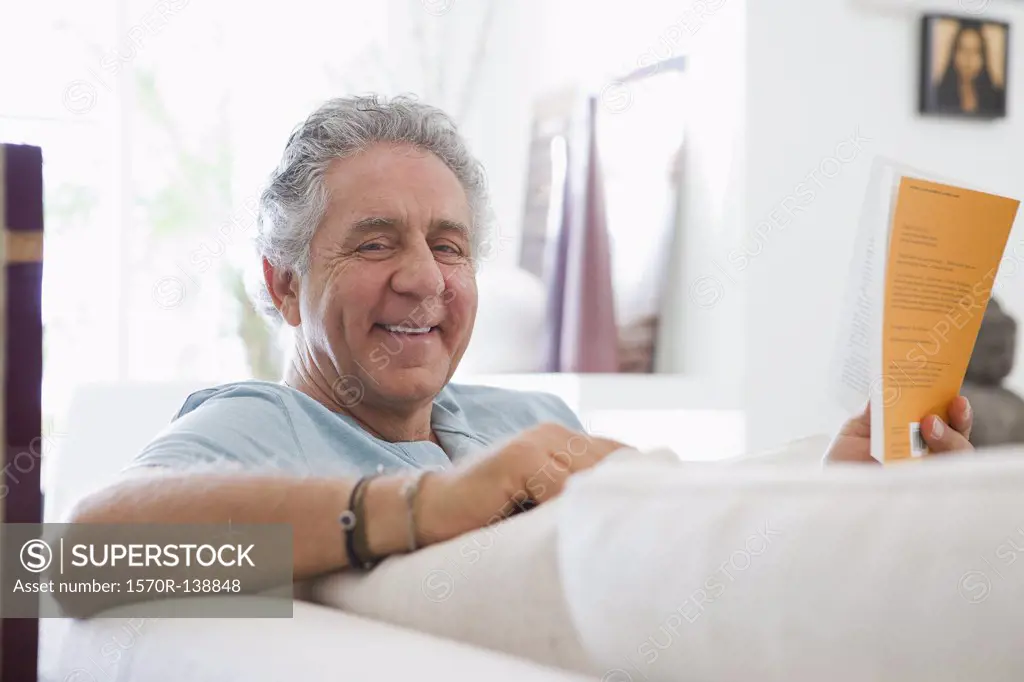 A cheerful senior man reading a book at home