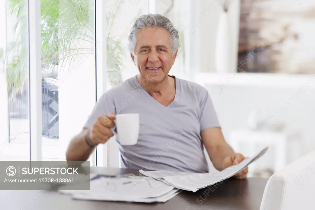 A cheerful senior man reading the paper and drinking coffee