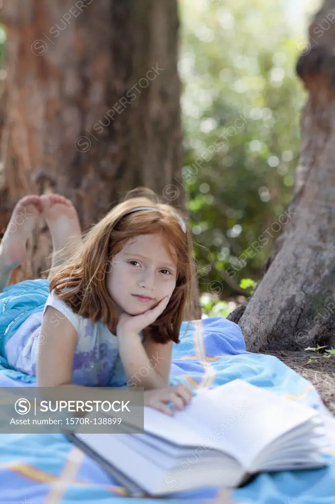 Girl lying on blanket in park with book