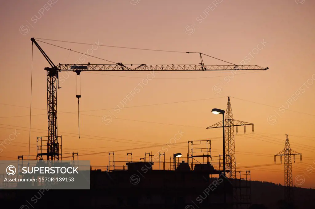 A construction crane and electricity pylons silhouetted against a sunset sky