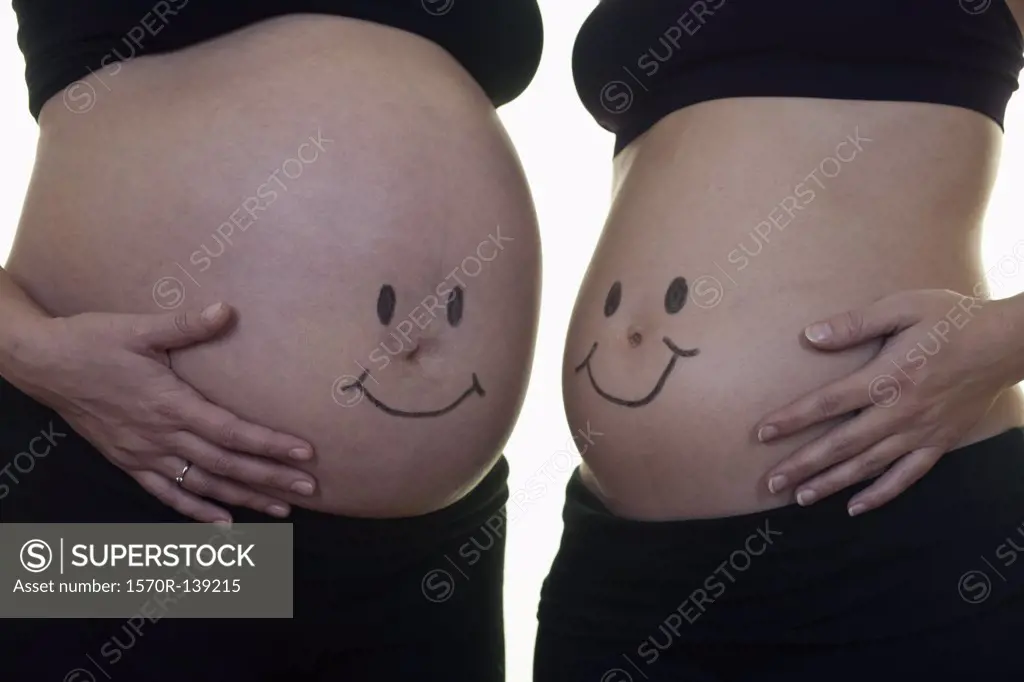 Two pregnant women with smiley faces on their bellies, midsection