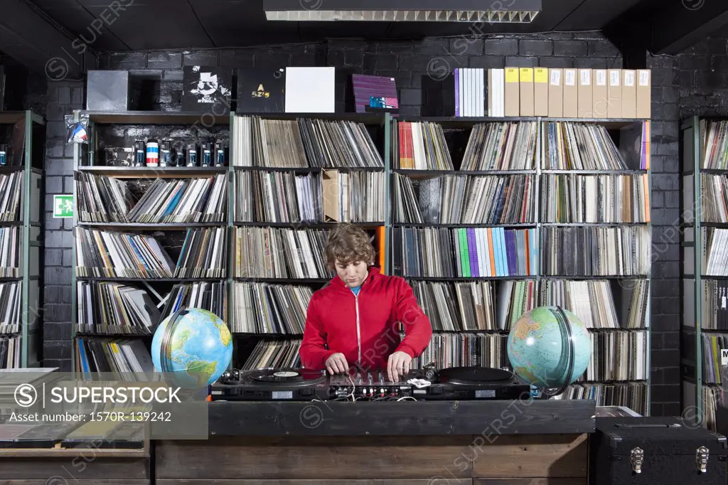 A young man using a sound mixer and DJ decks at a record store