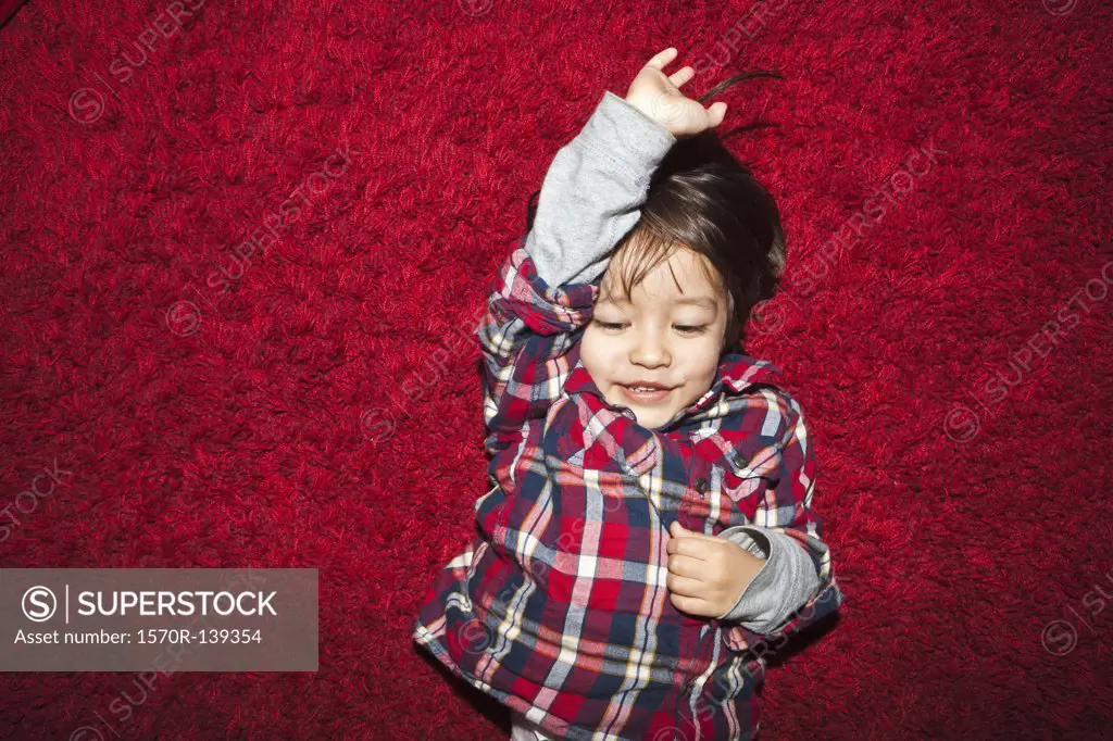 A young smiling boy lying on a red carpet