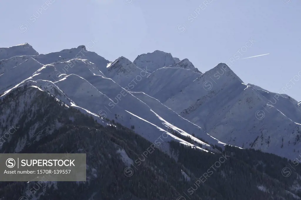 Snow-capped mountain range with vapor trail of plane in background