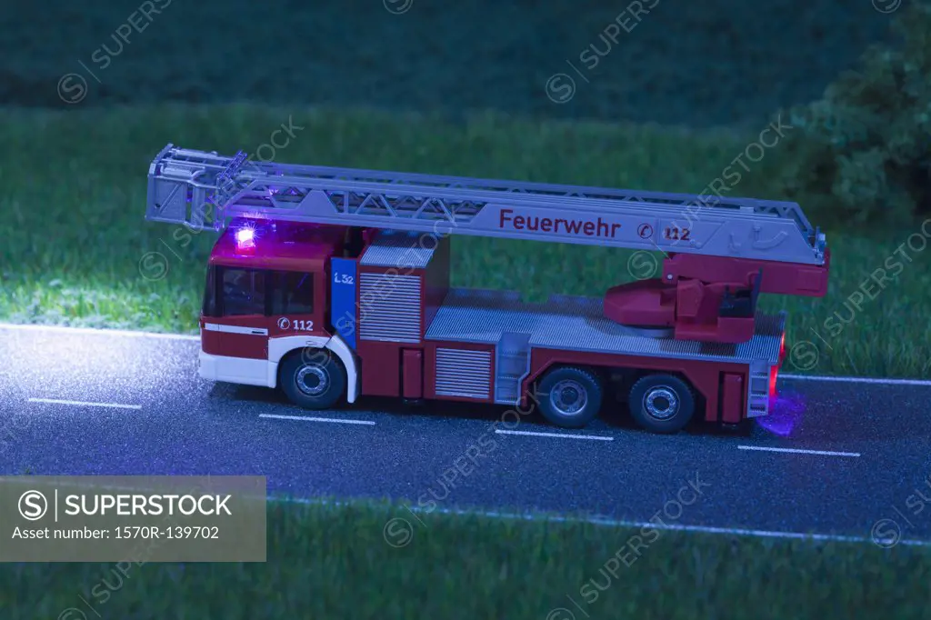 A diorama of a miniature toy fire truck driving on a road at night