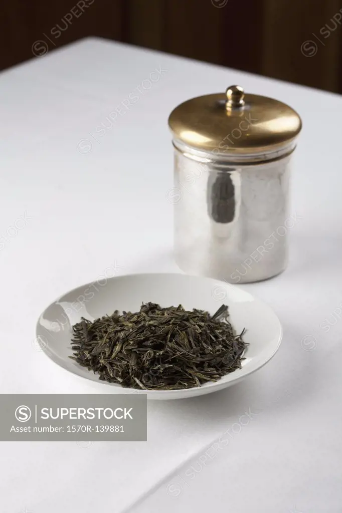Green tea leaves in a dish next to a canister