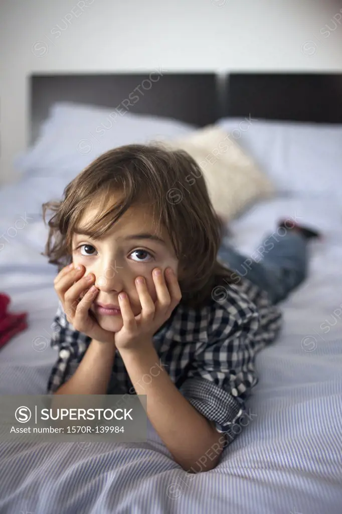 A young boy lying on a bed looking sad
