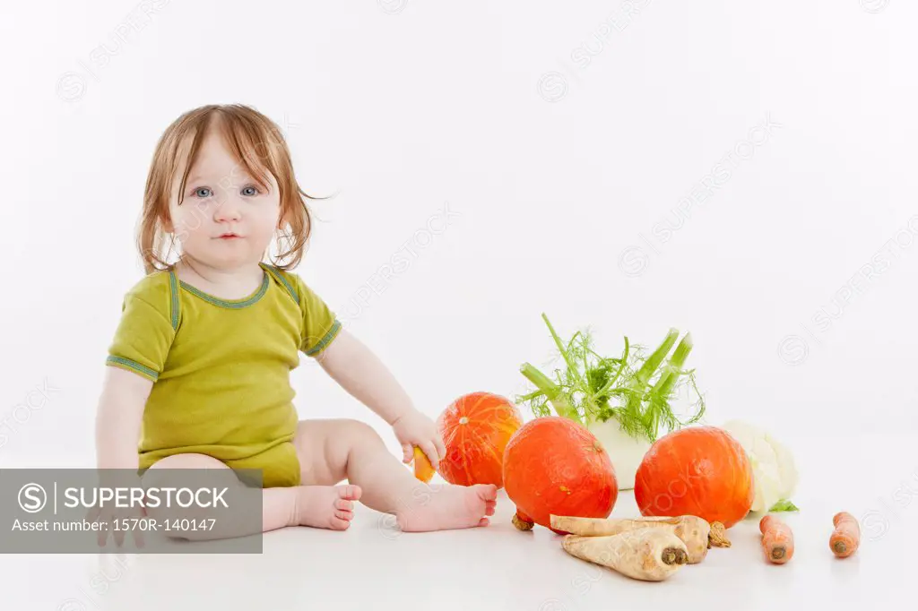 A baby girl sitting with vegetables