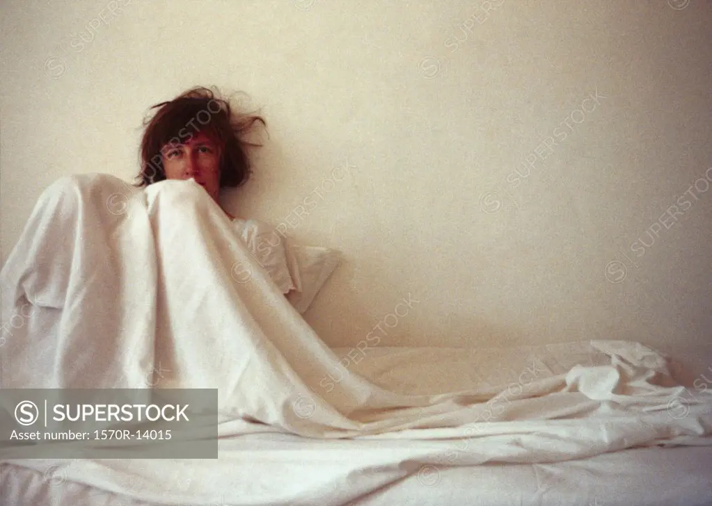 woman covered in sheets, leaning against the wall