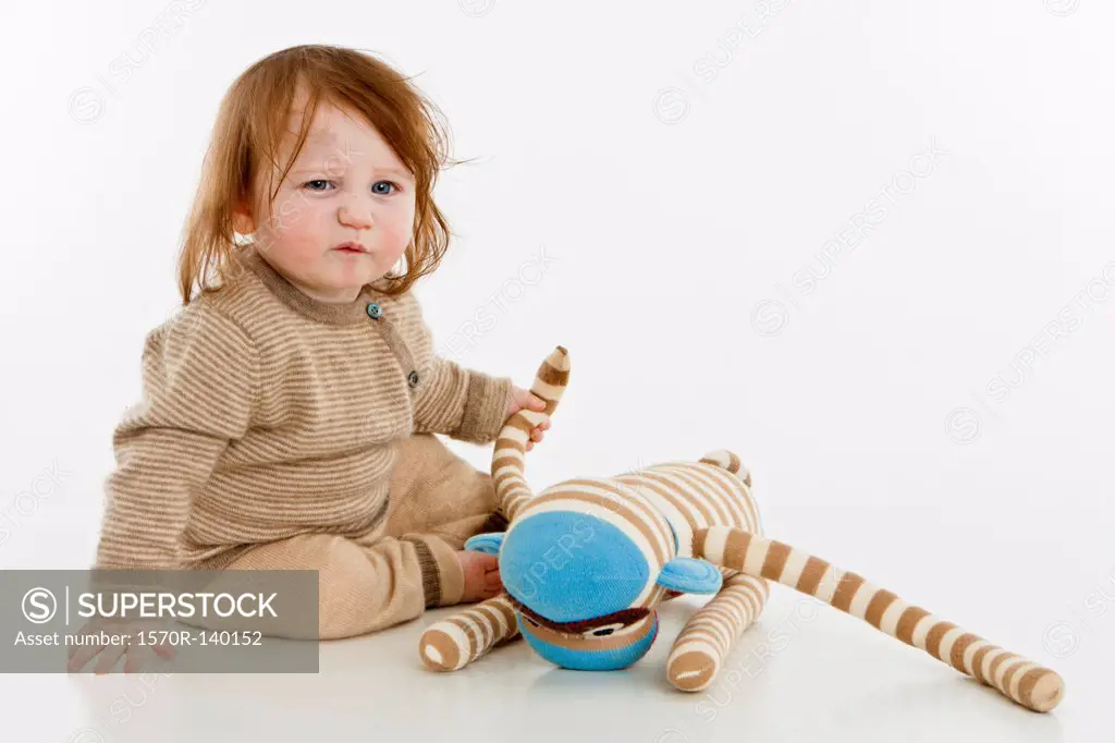 A baby girl sitting with a stuffed toy