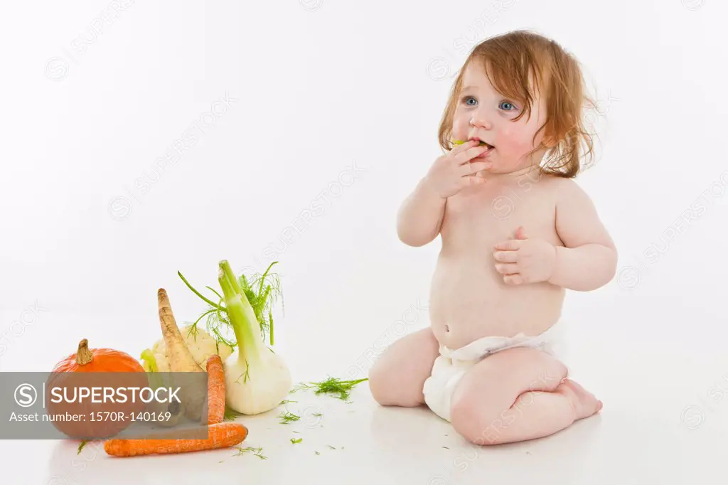 A baby girl next to vegetables