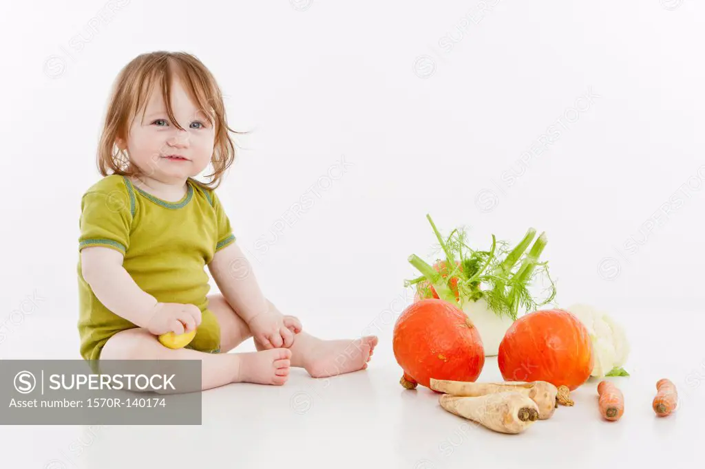 A baby girl sitting with vegetables