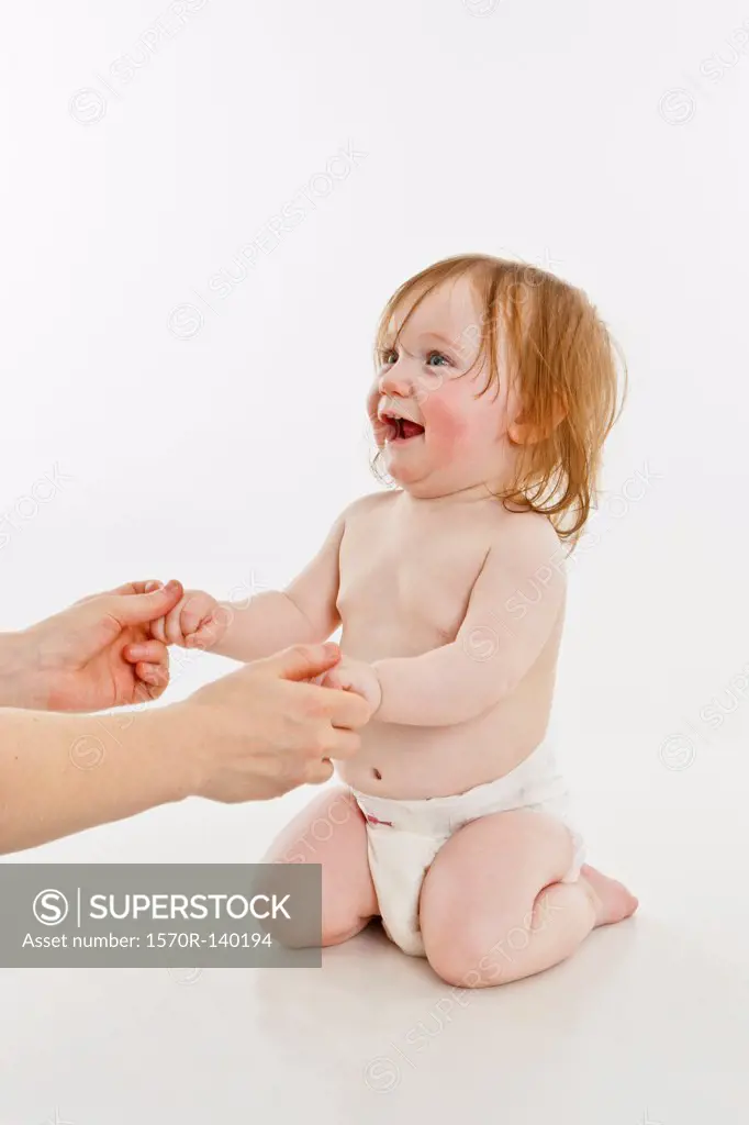 An adult holding the hands of a baby girl