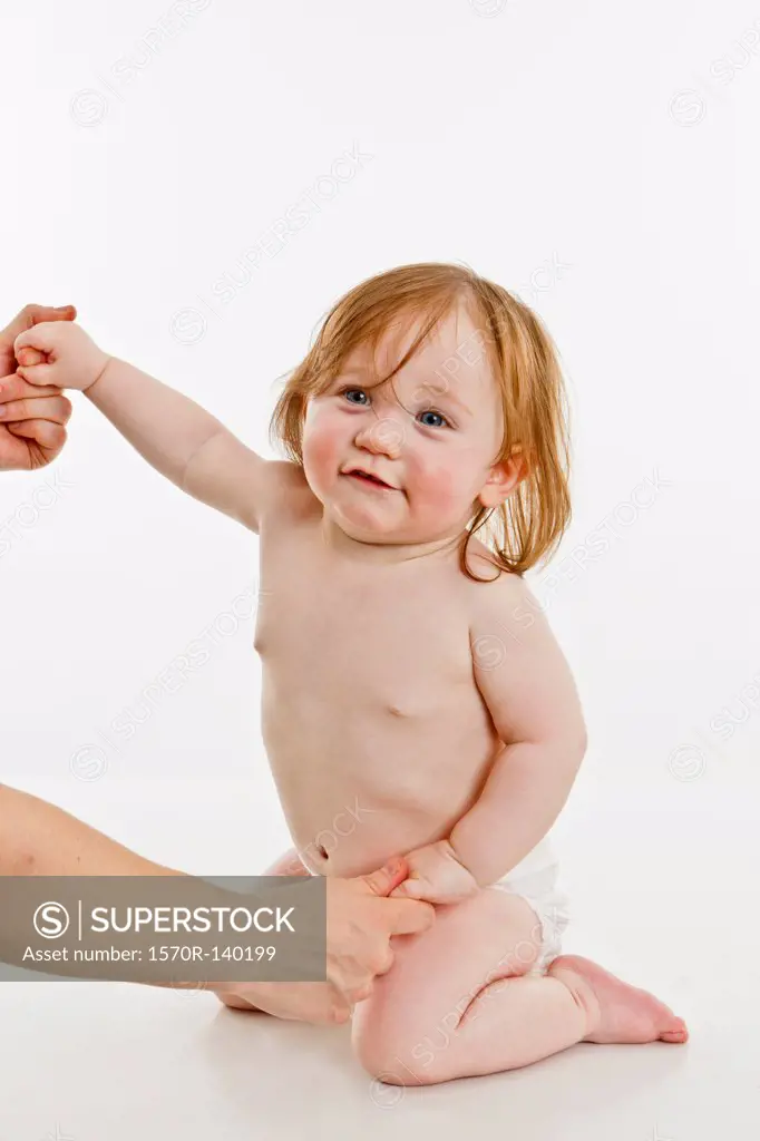 An adult holding the hands of a baby girl