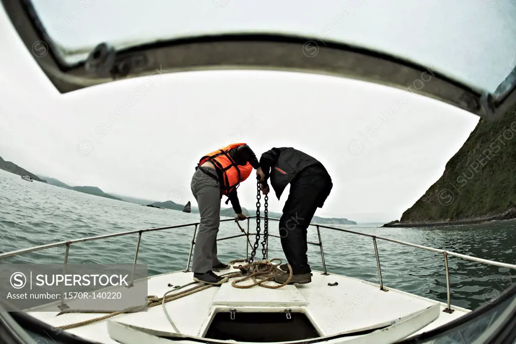 Two people engaged in lowering an anchor off the bow of a boat, Avacha Bay, Russia