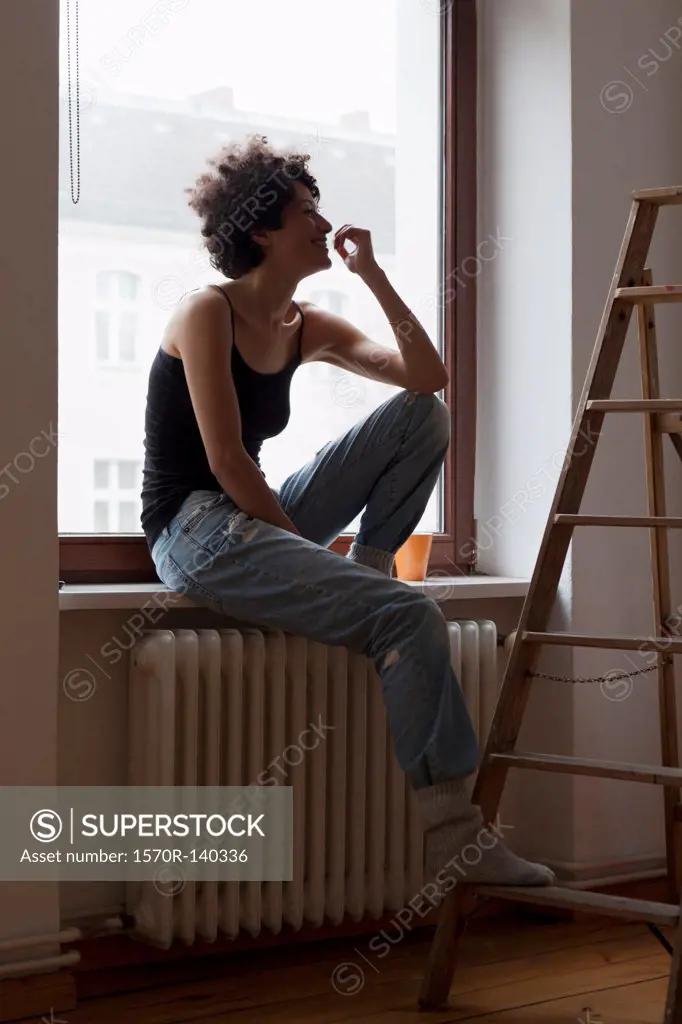 A woman sitting on a window sill and resting her foot on a ladder