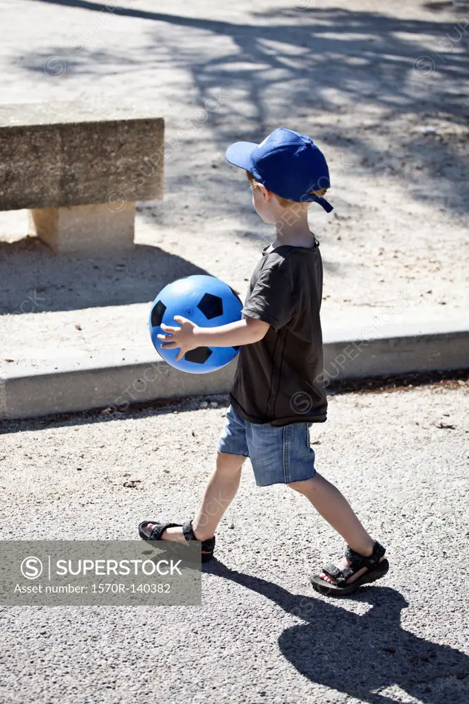 A young boy walking with a ball