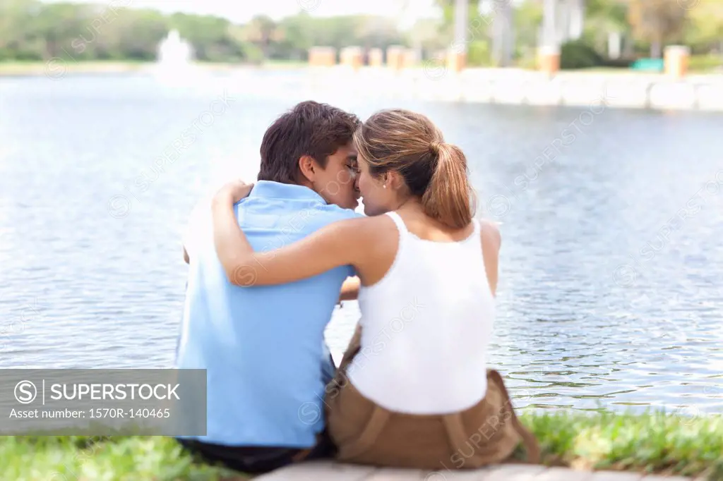 An affectionate couple kissing by a lake, rear view