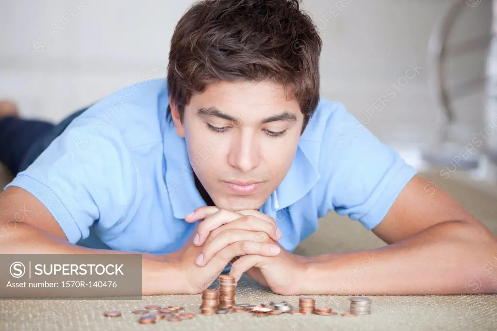 A man lying on a floor looking down at stacks of coins