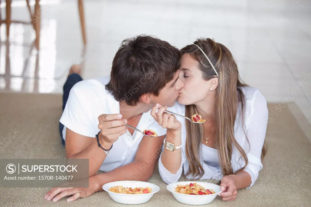 A young couple kissing while eating breakfast