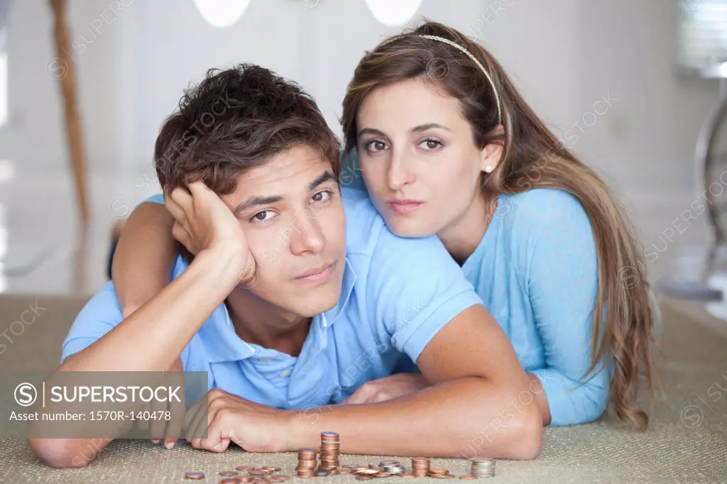 A young serious couple lying on the floor near stacks of coins