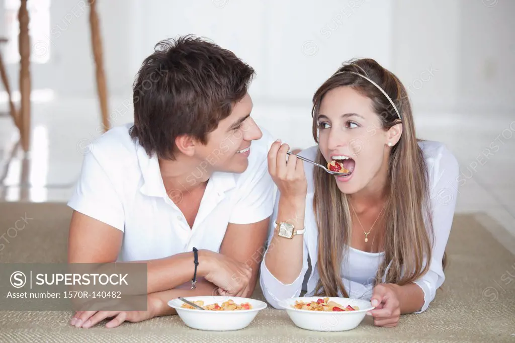 A young couple lying on the floor eating cereal for breakfast