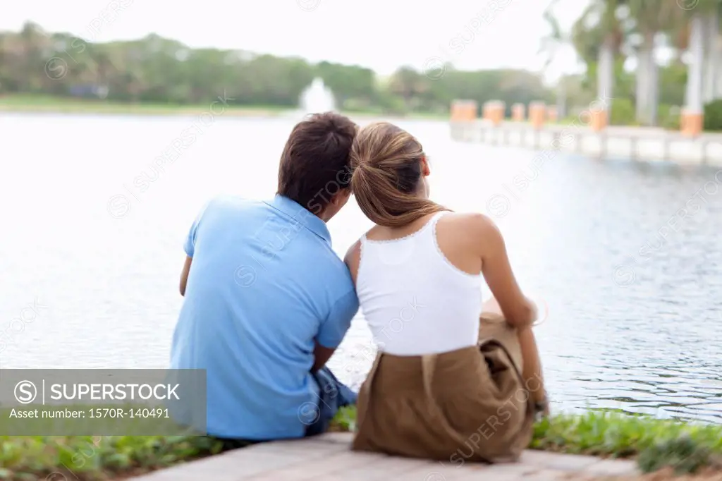 A couple sitting by a lake, rear view