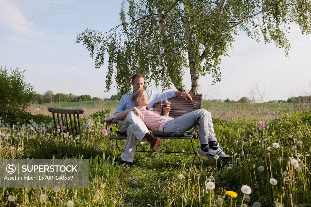 A couple enjoying sunshine and wine on a bench in their backyard