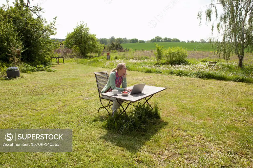 A woman with a laptop sitting at a table in her back yard, rural setting