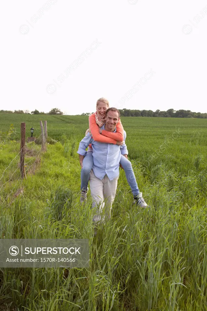 A man giving his girlfriend a piggy back ride through a field