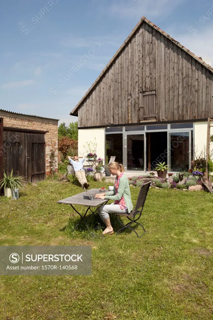 A woman using a laptop and having breakfast in her backyard