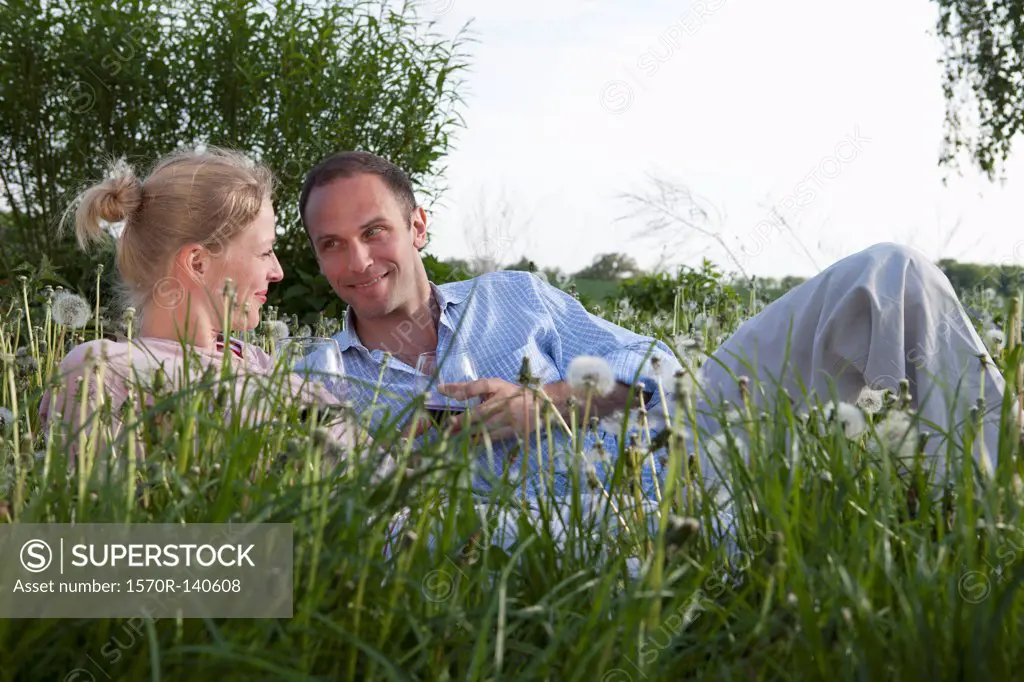A couple lying in the grass enjoying some red wine