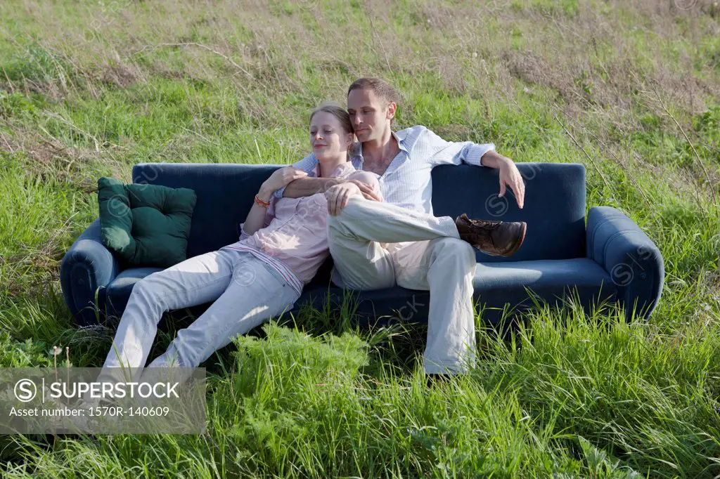 A couple sitting on a sofa in a field of grass