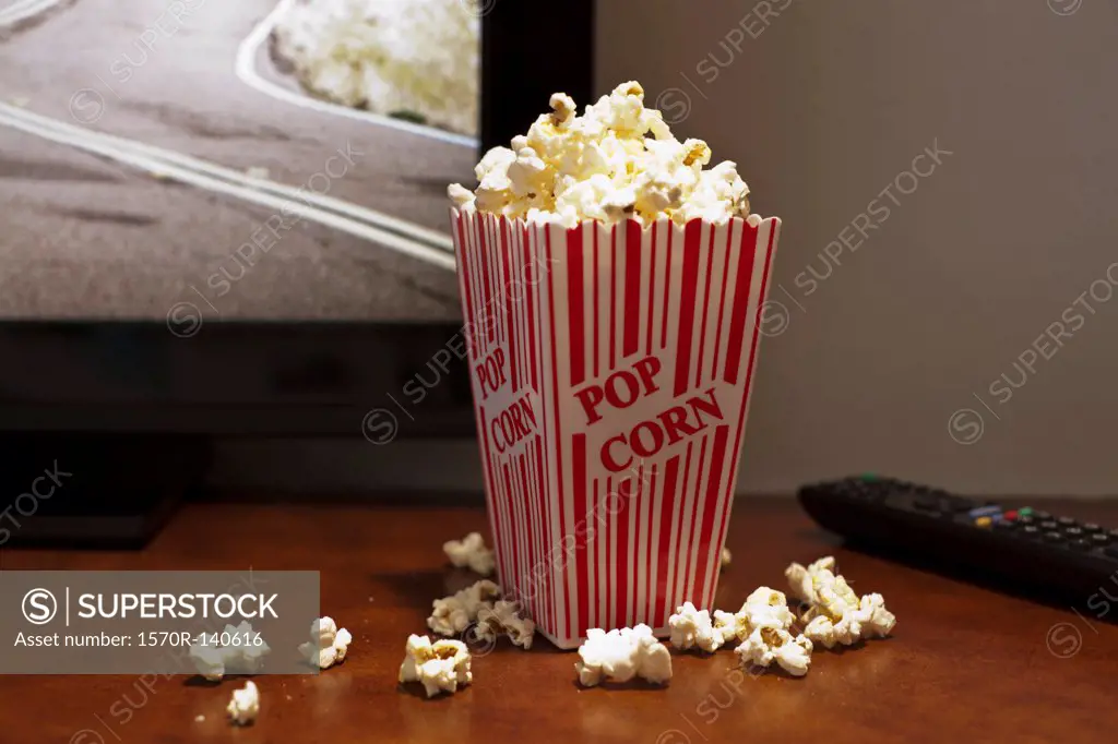 A red striped carton of popcorn on a table in front of a flat screen TV