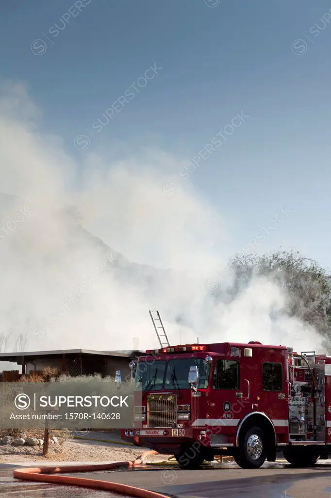 A fire truck next to a burning house in a suburb
