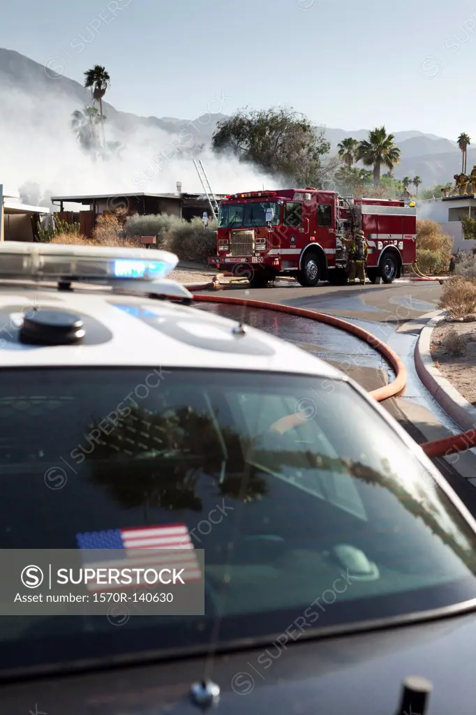 A police car and a fire truck at the scene of a burning house in a suburb