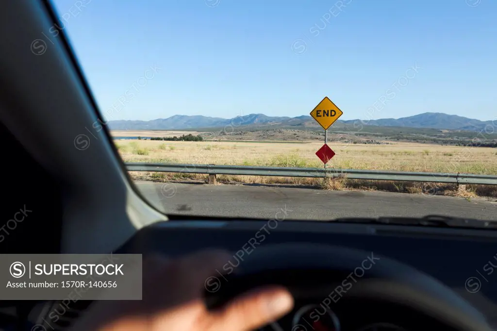 View through a car windshield of an END road sign and mountain ranges behind