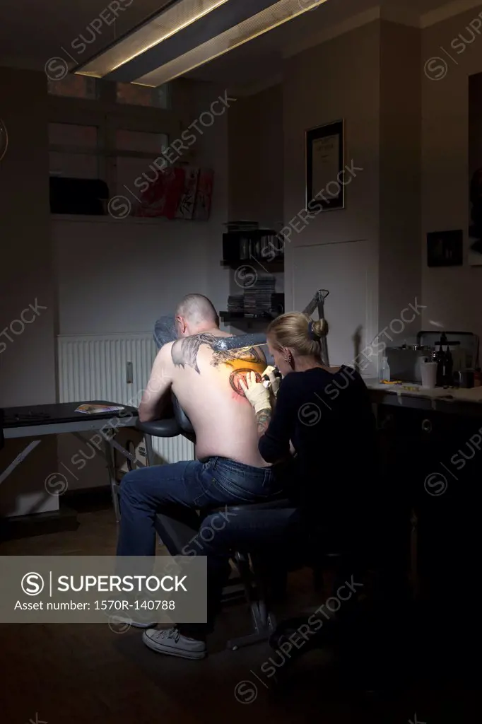 A female tattoo artist tattooing a man's back in a tattoo shop