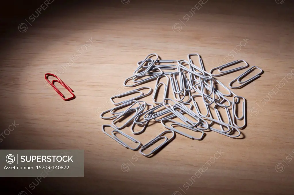 One red paperclip set apart from a heap of white paperclips
