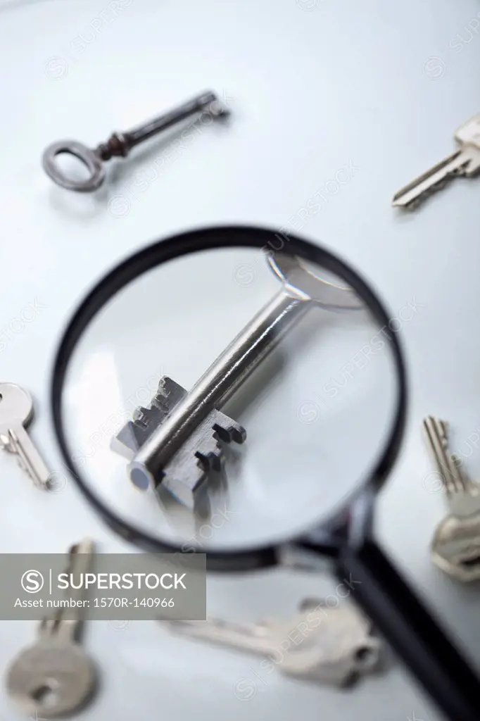 A key lying amongst many being magnified by a magnifying glass