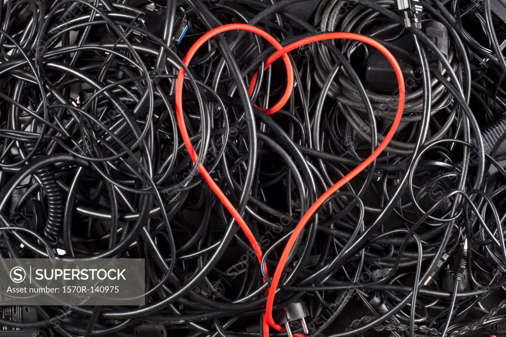 A red cord in a heart shape amongst tangled black cables and cords